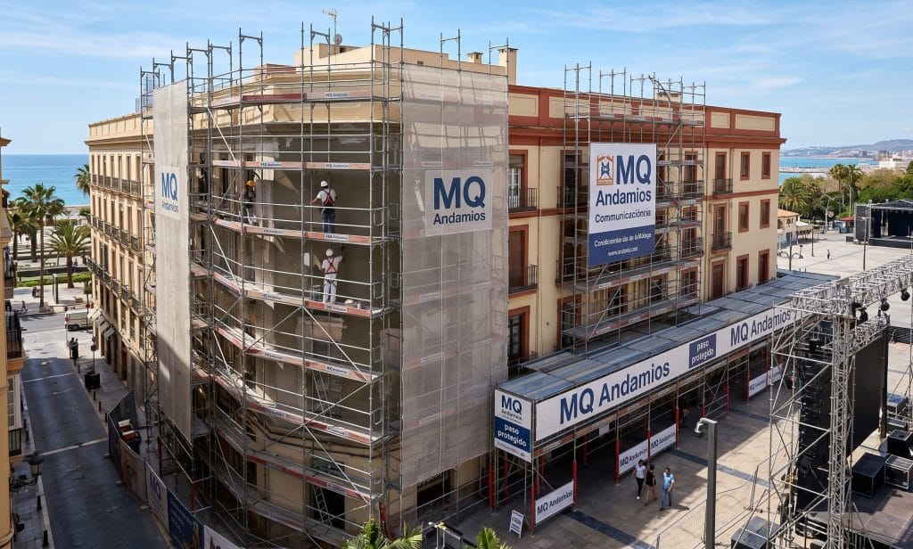 Operarios montando una estructura de andamio en Málaga, con un banner de la empresa MQ Andamios visible.